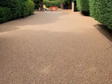 Long golden resin driveway between tall hedges